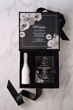 an open box containing a bottle of wine and some black ribbon on a white marble surface