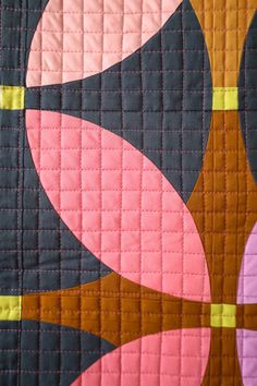 a quilted wall hanging with an abstract design on it's side and pink, black, yellow, and orange colors