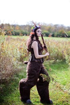 a woman dressed as a bear with horns and antlers on her head is standing in the grass