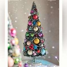 a small christmas tree made out of beads and other ornaments in front of a gray background