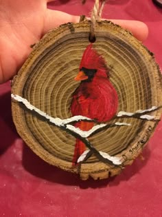 a hand holding a piece of wood with a red bird painted on it