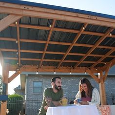 a man and woman sitting at a table under a pergolated roof with an awning