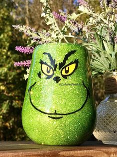 a green grin face mug sitting on top of a table next to a vase filled with flowers