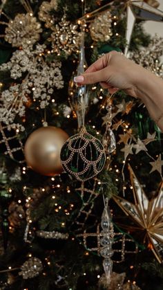 a person holding an ornament in front of a christmas tree with ornaments on it