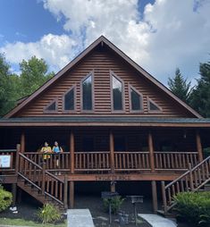 two people are standing on the porch of a log cabin with stairs leading up to it