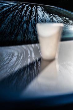 a white cup sitting on top of a table next to a car window with trees reflected in it