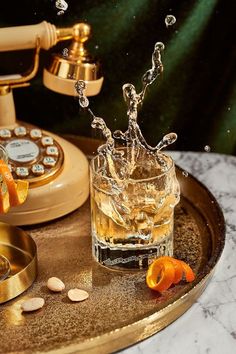 an orange splashing into a glass on top of a tray next to a phone