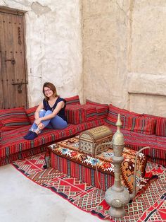 a woman sitting on top of a red couch next to a table with a lamp