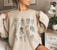 This jellyfish sweater with a jellyfish print is perfect for an ocean inspired style and summer sweatshirt for animal, marine life, sea and nature lovers. It's a great gift for marine biologists. Also available as T-Shirt: https://wandercraftsdesign.etsy.com/listing/1728681053/save-the-ocean-inspired-style-jellyfish ♥PRODUCTION TIME: 1-5 days (usually 2-3 days) ♥SHIPPING TIME: 2-5 days in USA (Usually 2-3 days). International shipping takes longer. ♥PRODUCT DESCRIPTION: Gildan 18000 Unisex Sweat Jellyfish Sweater, Work Appropriate Costumes, Jellyfish Shirt, Sweater Print, Save The Ocean, Jellyfish Print, Summer Sweatshirt, Underwater Sea, Animal Nature