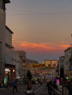 people are walking down the street in front of some buildings at sunset or sunrise time