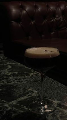 a drink sitting on top of a table next to a brown leather couch in a dark room