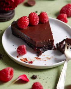 a piece of chocolate cake on a plate with raspberries next to it and a fork