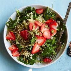 a white bowl filled with salad and topped with sliced strawberries on top of a blue table