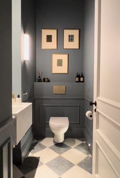 a white toilet sitting inside of a bathroom next to a sink and mirror with pictures on the wall