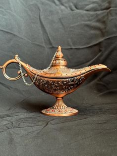 an ornately decorated teapot on a black cloth covered table with a chain hanging from the handle