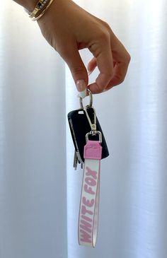 a hand holding a keychain that has a pink and white lanyard attached to it