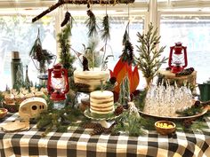 a table topped with lots of cakes and desserts next to a window covered in pine cones