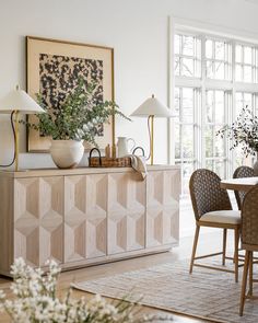 a dining room table and chairs in front of a large window with white vases on it