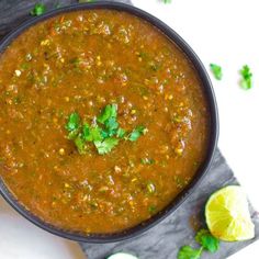 a bowl of chili with cilantro and lime on the side next to a spoon