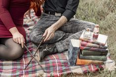 a man and woman are sitting on a blanket with books in front of their feet