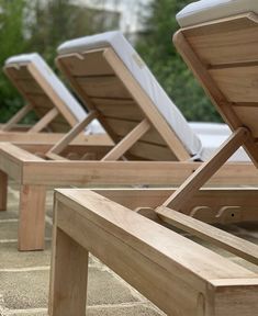 three wooden lounge chairs sitting next to each other on top of a stone patio area