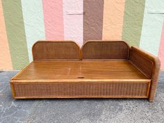 a wooden bed sitting on top of a sidewalk next to a wall with multicolored stripes