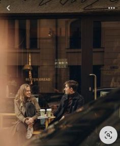 two people sitting at a table in front of a store window with the reflection of another man and woman