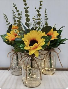 three mason jars with sunflowers and greenery in them