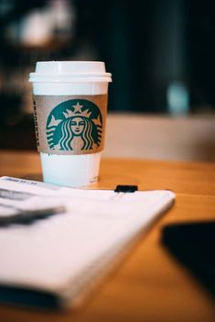 a cup of coffee sitting on top of a table next to a notebook and pen