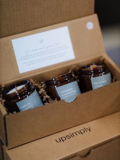 three jars of candles in a box on top of a wooden table with the words upsismmoy printed on it