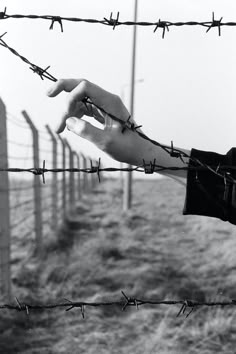 a hand reaching out from behind a barbed wire fence