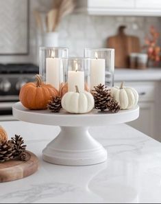 a white cake plate topped with candles and pine cones on top of a kitchen counter