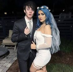 a man in a suit standing next to a woman with blue hair and makeup on