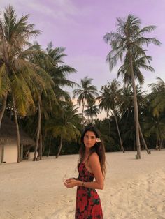 a woman in a red and black dress standing on the beach next to palm trees