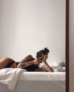 a woman laying on top of a bed looking at her cell phone in the mirror