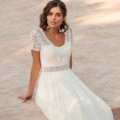 a woman in a white dress is sitting on the sand and posing for a photo