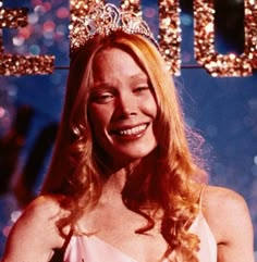 a woman wearing a tiara and smiling at the camera while standing in front of a sign