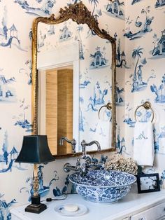 a bathroom with blue and white wallpaper has a large mirror above the sink, along with a lamp