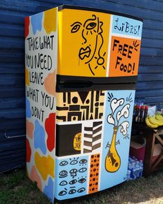 a colorful refrigerator sitting in the grass next to a blue wall with writing on it