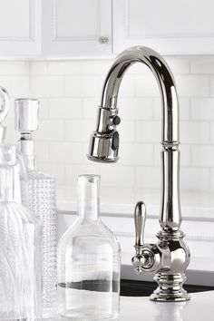 a kitchen sink with bottles and glasses on the counter next to it, including an old fashioned faucet