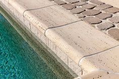 a bird sitting on the edge of a swimming pool next to a stone wall and walkway