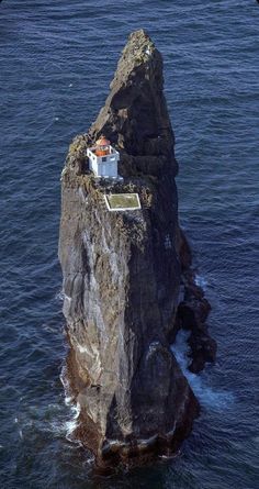 an aerial view of a small house on top of a rock in the middle of the ocean