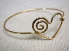 a close up of a gold bracelet on a white surface with a spiral design in the middle