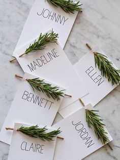 four place cards with rosemary on them are sitting on a marble countertop and the names of each card