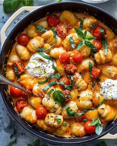 a skillet filled with pasta, tomatoes and mozzarella on top of a table