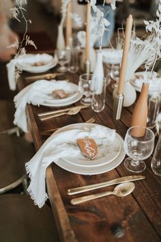 a wooden table topped with white plates and silverware