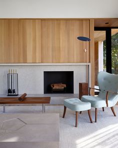 a living room with two chairs and a fireplace in the center, surrounded by wood paneling