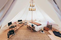 a bed sitting inside of a white tent next to a wooden table and two chairs