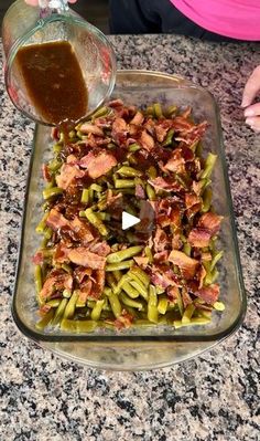 someone is pouring gravy over green beans in a glass dish on the counter