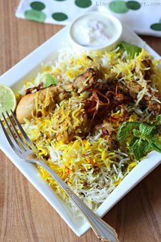 a white plate topped with rice and meat next to a fork on top of a wooden table